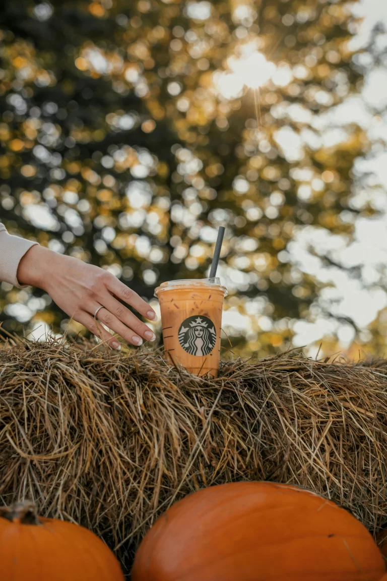 Woman reaching for Starbucks pumpkin spice latte. With a crisp fall day, hay and pumpkins as a background.